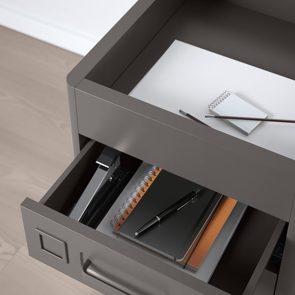 Grey metal drawer unit with pen, notebook, and binder inside; designed for office use with integrated dampers for silent closure.
