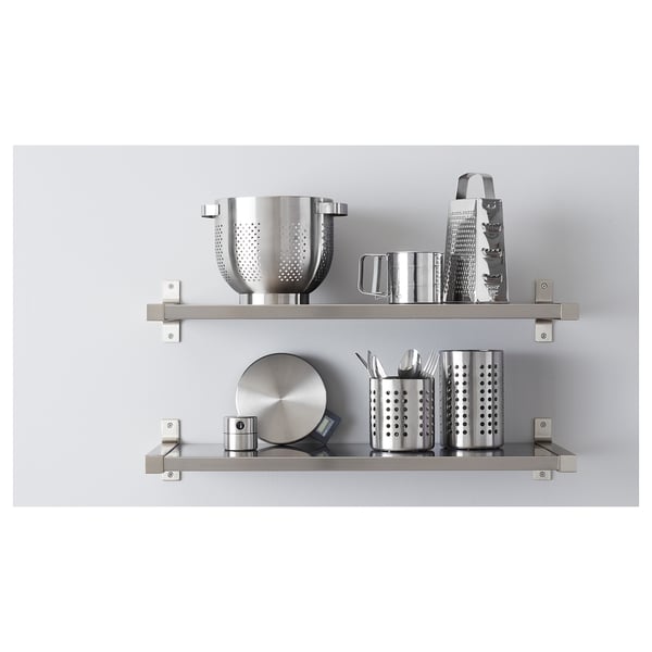 Stainless steel kitchen utensils organised on two wall shelves including a bowl, grater, containers, and pans.