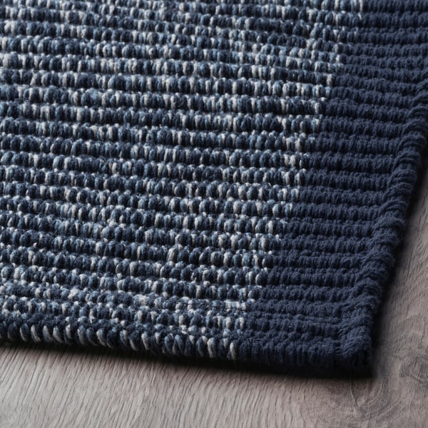 Dark blue textured cotton rug, folded on wooden floor. Soft, high-quality material, neatly stitched edges.