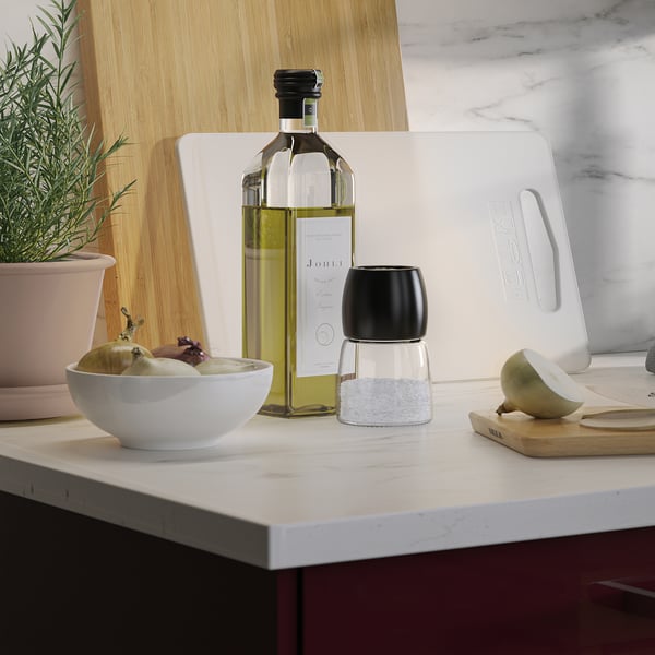 On kitchen counter, bowl with fruit sits near bottle of oil and grinder.