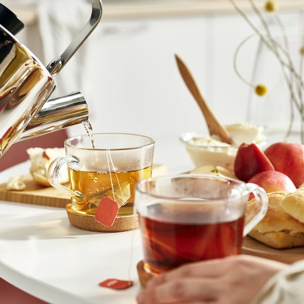 Tea cups on coasters, kettle pouring tea, pastries.