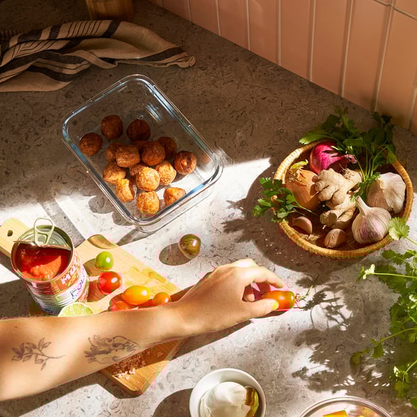 A person chops tomatoes on a cutting board next to roasted veggies and fresh produce, showcasing food prep and storage.