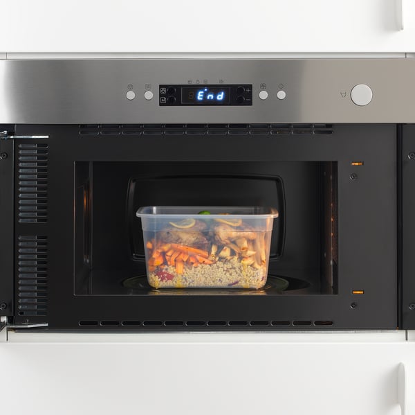 Stainless steel microwave with illuminated end display, heating food in a transparent plastic container.