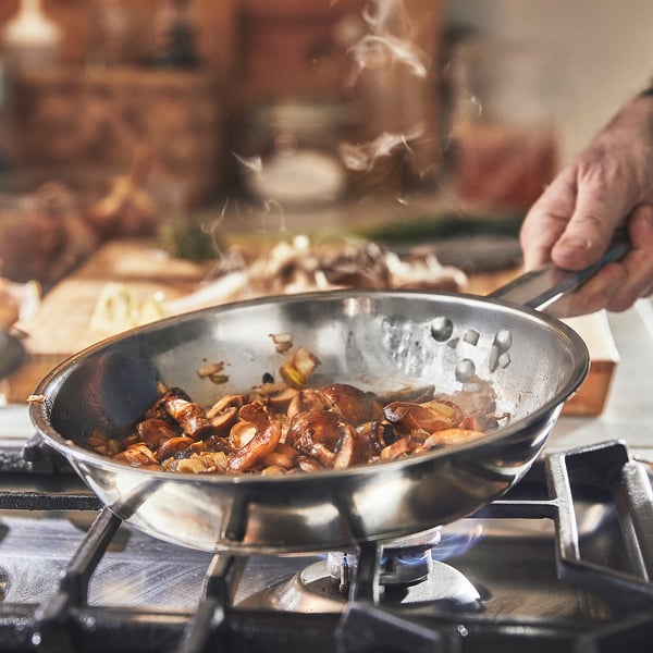 Cooking mushrooms in stainless-steel pan on gas stove.