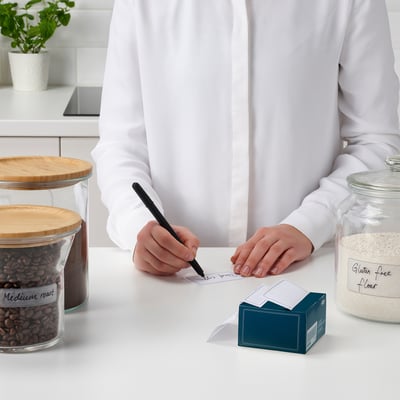 Person writing on label near jars of coffee and flour in kitchen.