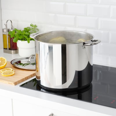 Large stainless cookpot with handles sits on modern stove, boiling food; placed in clean, minimalist kitchen.