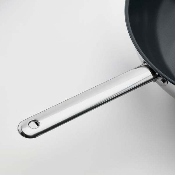 Shiny, modern wok handle made of stainless steel, attached securely to a non-stick pan.