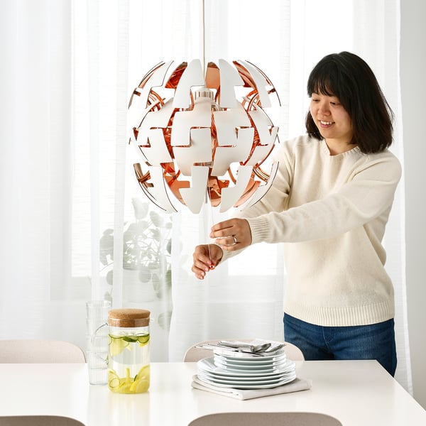 Person adjusts hanging lamps light intensity, with stacked dishes and a jug on table.