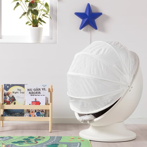 Cosy white IKEA PS LÖMSK kids armchair with hood, next to bookshelf with colourful books, blue star light, and green plant.