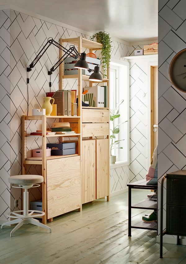 Bright room with IVAR light wood shelves, desk, and stool. Black lamps, colourful decor, and wall plants. White door, patterned wall.