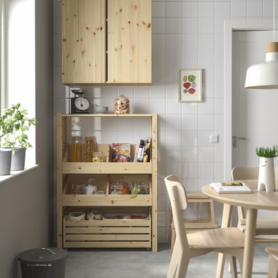 Light wood IVAR shelving unit holds pantry items near dining area. Tall, narrow, fits under cabinets.