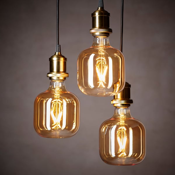 Three vintage-style light bulbs hang from fabric cords, glowing warmly against a grey background.