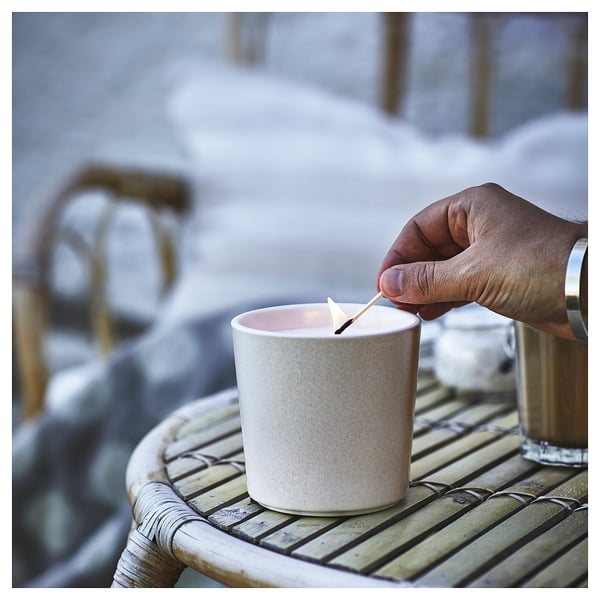 Hand lights JÄMLIK candle on bamboo table, ceramic jar.