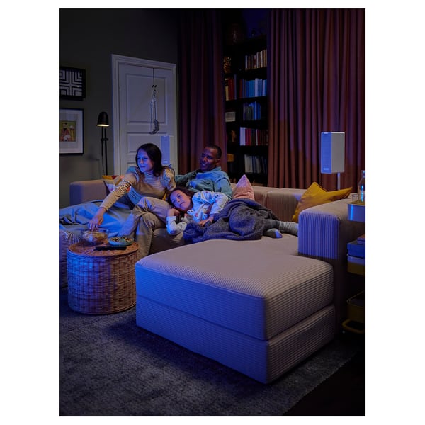Three people relax on a JÄTTEBO modular sofa in a cosy living room, featuring large pillows and blankets, with a stylish bookshelf in the background.