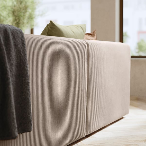 Modern white cushioned sofa with green pillow, grey blanket, wooden floor, window view, and cat.