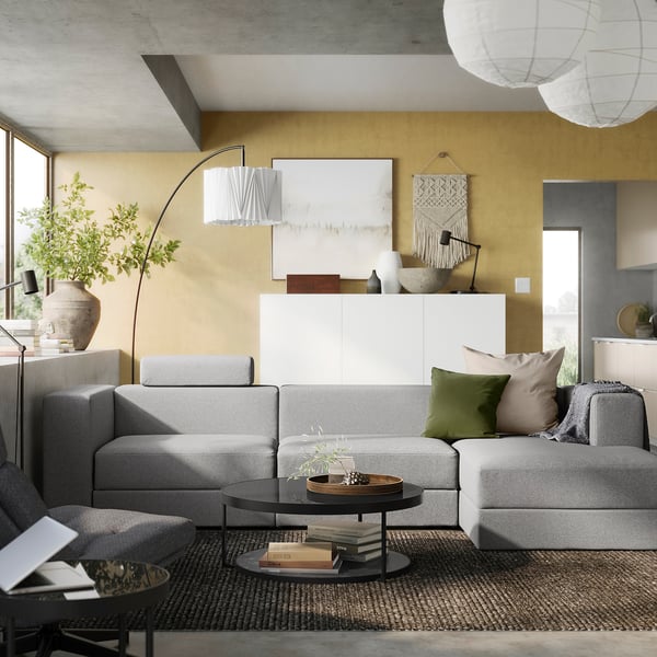 Modern living room with a grey JÄTTEBO modular sofa, green pillows, wooden coffee table, and mustard yellow walls, featuring a contemporary design.