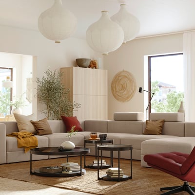 Cosy living room with beige modular sofa, red accent chair, hanging lanterns, and large window providing natural light.