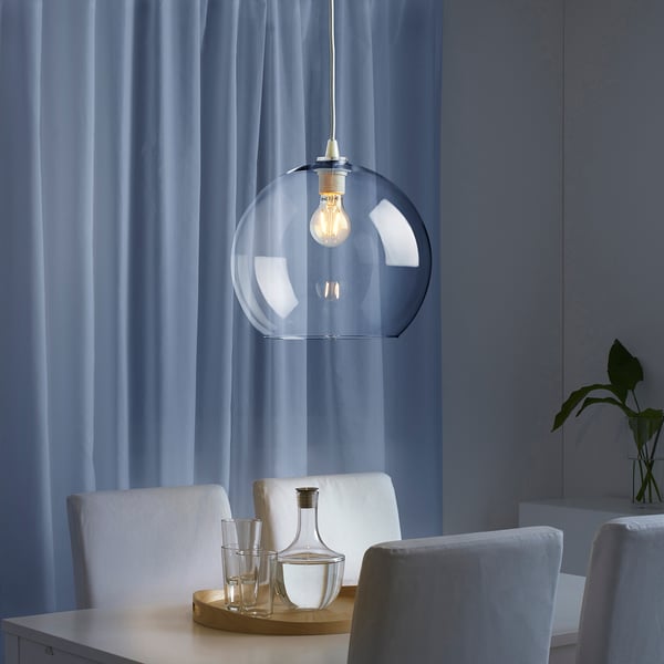 Hanging light fixture with glass shade, bulb lit, above table with chairs and glassware.