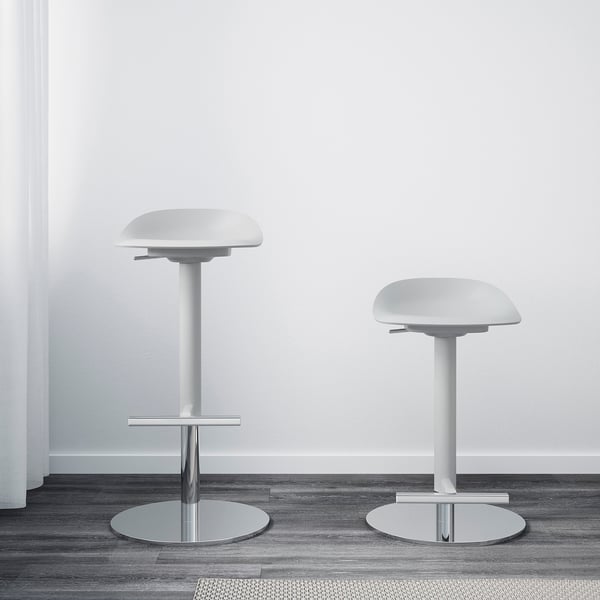 Two white bar stools with round seats and chrome bases; one has a footrest, both adjustable heights.