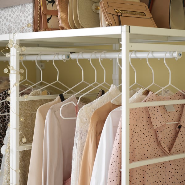 White JONAXEL wardrobe with beige shelves; light pink, white, and dotted blouses hang neatly, adorned with string lights.