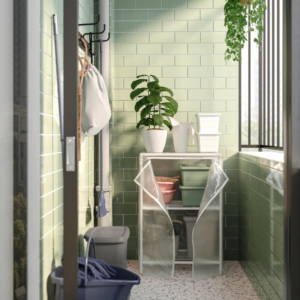 Balcony shelving unit with green tiles, white bins, and potted plants. Transparent cover protects items.