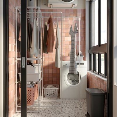 Laundry room with white JOSTEIN storage, drying rack, and washing machine. Clothes hang and sit in baskets, tiled walls.