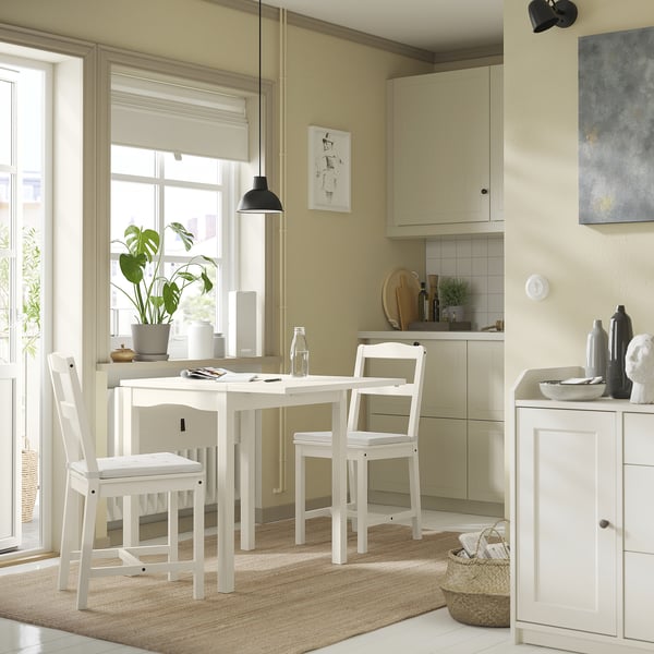 Cosy kitchen nook with JUSTINA white chairs, beige rug, green plant, and light wood cabinets.