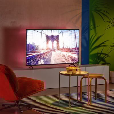 Modern tv room with colourful decor, large screen, orange chair, vibrant walls, led lighting, small table with snacks.