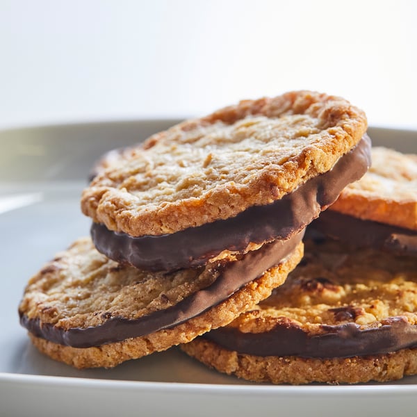 Stacked golden-brown oat cookies with dark chocolate filling on a white plate.