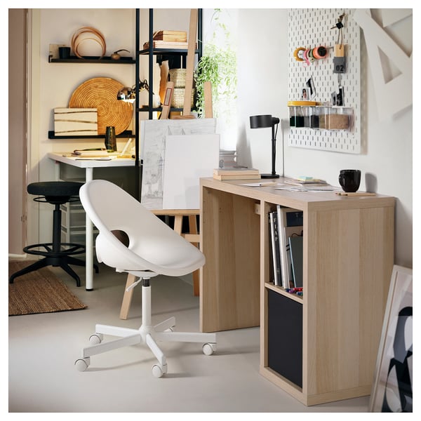 Modern home office with KALLAX light wood desk, white chair, and storage solutions.