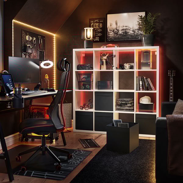 Modern home office with black & red desk chair, led-lit white KALLAX shelving unit, guitar, and tech gear.
