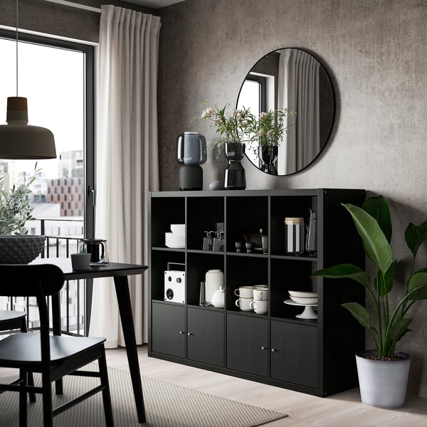 Modern dining area with black KALLAX shelving unit, large round mirror, black dining table, chairs, and plants.