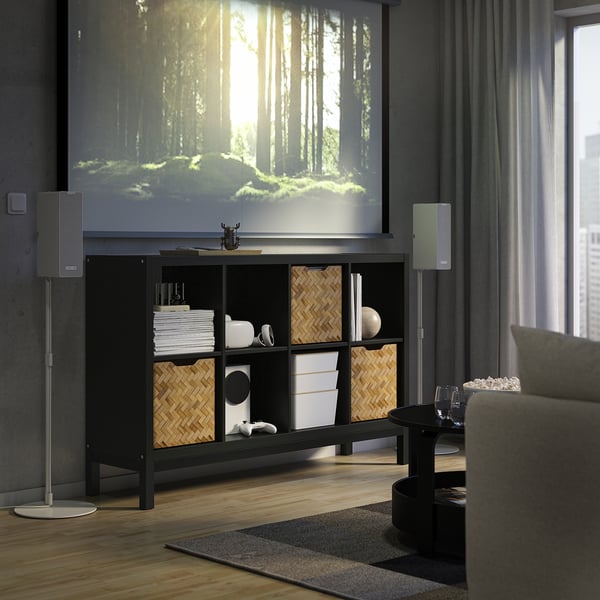 Modern living room with KALLAX sideboard, grey speakers, projected forest, cosy couch, wooden floor, and curtains.