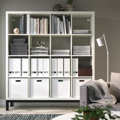 KALLAX white shelving unit organised with books, boxes, and decor. Tall, airy design, serves as room divider. Holds multiple items neatly.