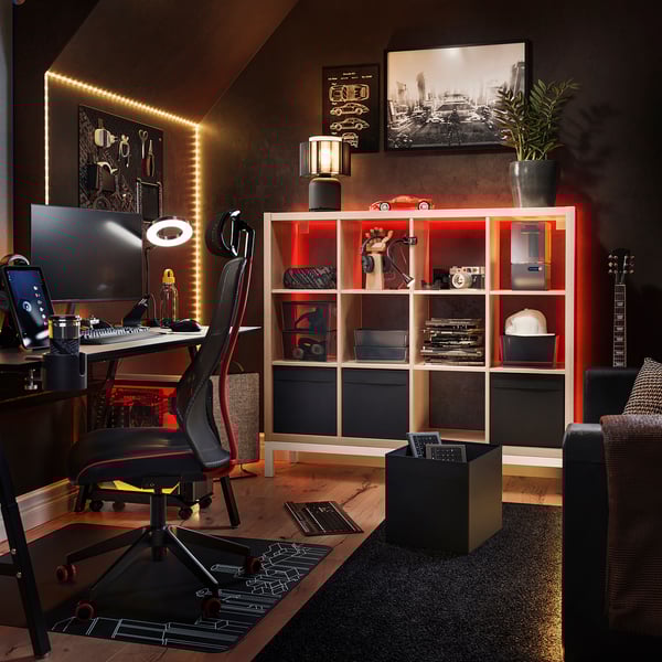 Modern office with KALLAX shelves, black and red accents, wooden floor, dark walls, computer setup, guitar, and decorative items.