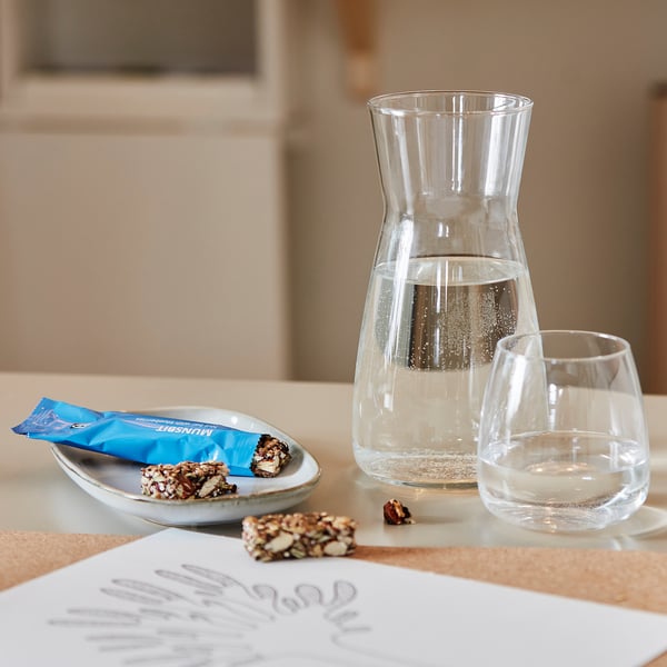 Glass carafe and glass with water, small plate with snack, menu on table.