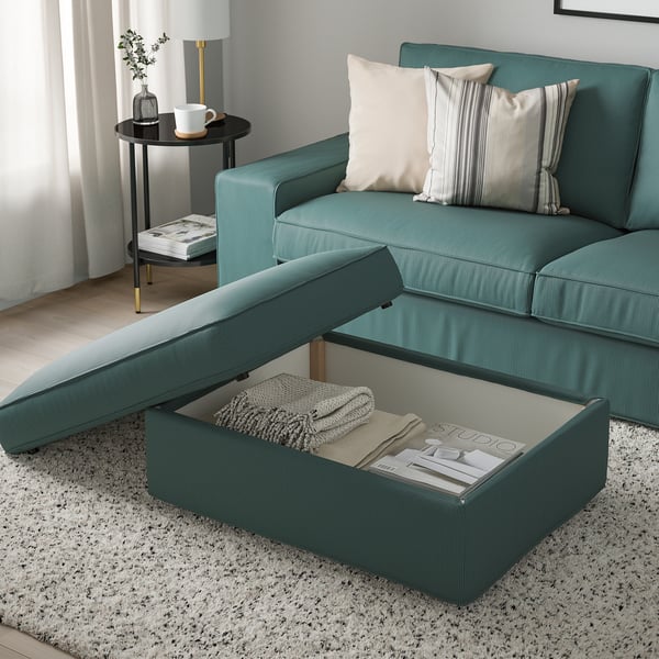 Green KIVIK footstool with storage under seat, on speckled rug, paired with green sofa, two blankets inside.
