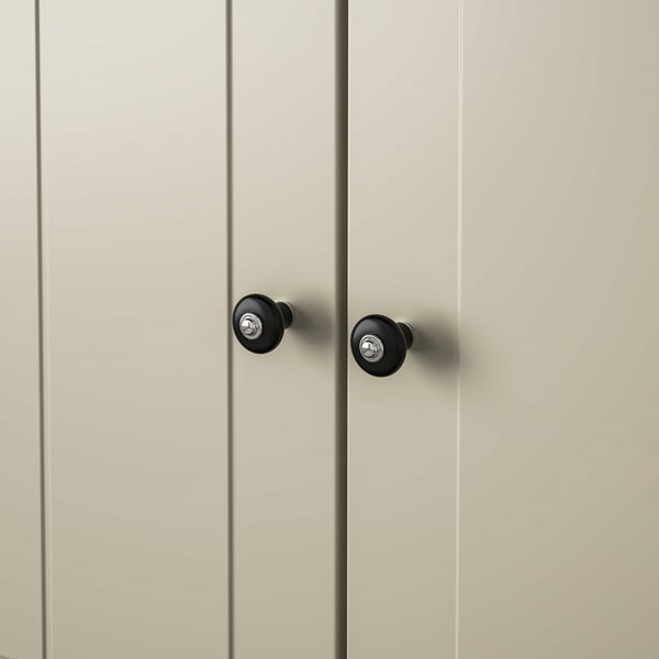 Close-up of two modern, matte black cabinet knobs with chrome fixing screws on a pale wooden door.