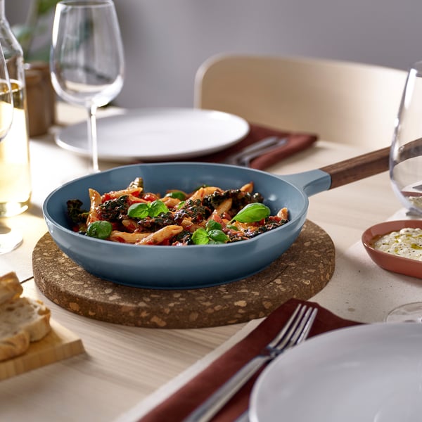 Meal in blue frying pan on table with plates, glasses, cutlery.