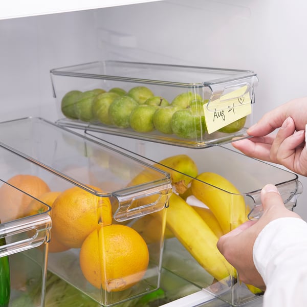 A hand accessing clear fridge drawers with fruits. Top drawer has a note: aug 21.