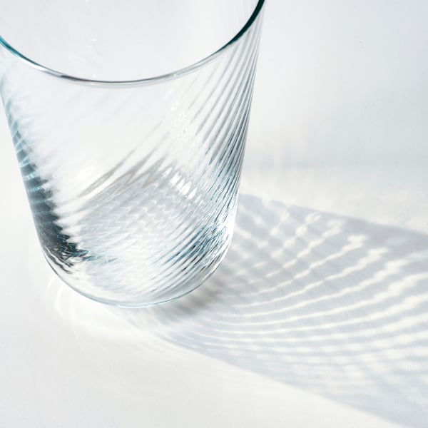 Elegant, thin glass on white surface, sunlight casts intricate rippled shadows.