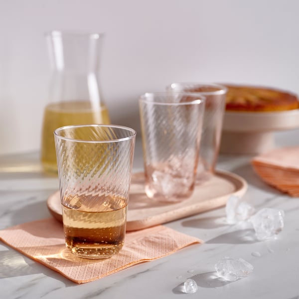 KLIPPLAX glass: clear w/ textured interior, slender, sits on pink napkin, surrounded by ice cubes.