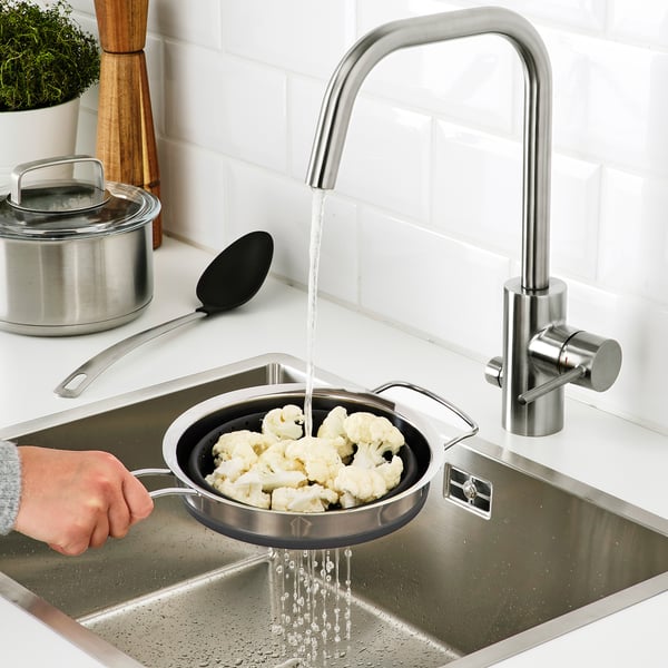 Person rinses cauliflower in adjustable steel colander under modern kitchen tap.