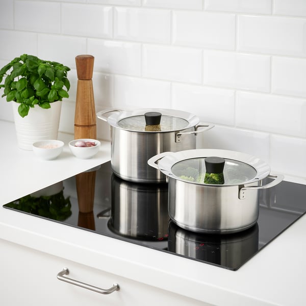 Two pots with glass lids on a black stove, one with broccoli, modern kitchen setting.