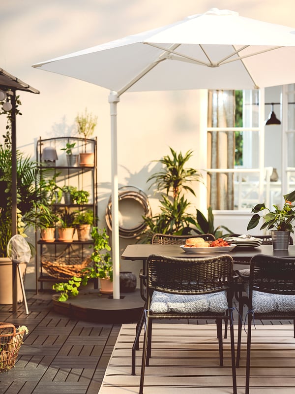 Patio with umbrella, food, chairs, plants, rug.