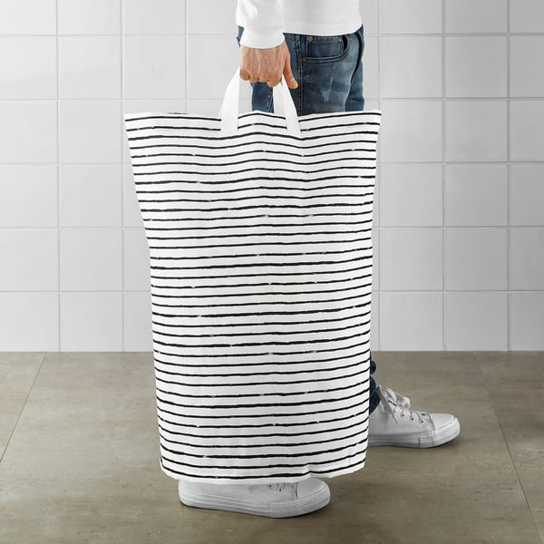 Person holding tall striped laundry basket by handles. Basket stands upright on its own.