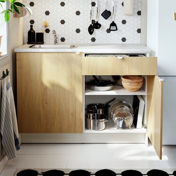 Kitchen cabinet with open drawer, showing organised pots, pans, and utensils. White counter, wood finish, hexagonal backsplash.