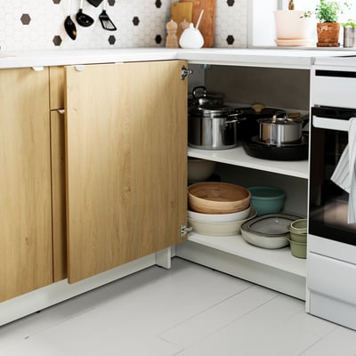 Kitchen cabinet with wooden door open, displaying pots, pans, and bowls neatly organised on adjustable shelves.