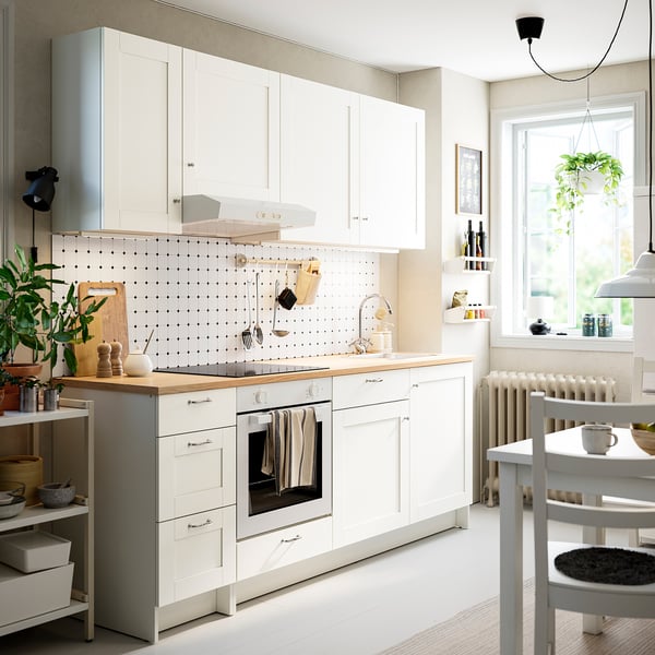 Modern white kitchen with wooden counter, storage, oven, shelves, plants, clean workspace.