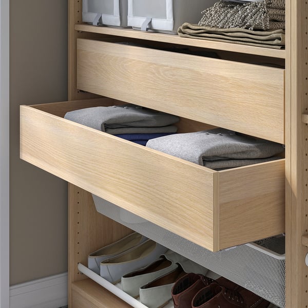 An open wooden drawer from IKEAs KOMPLEMENT series, filled with folded grey sweaters in a light-colored wardrobe.